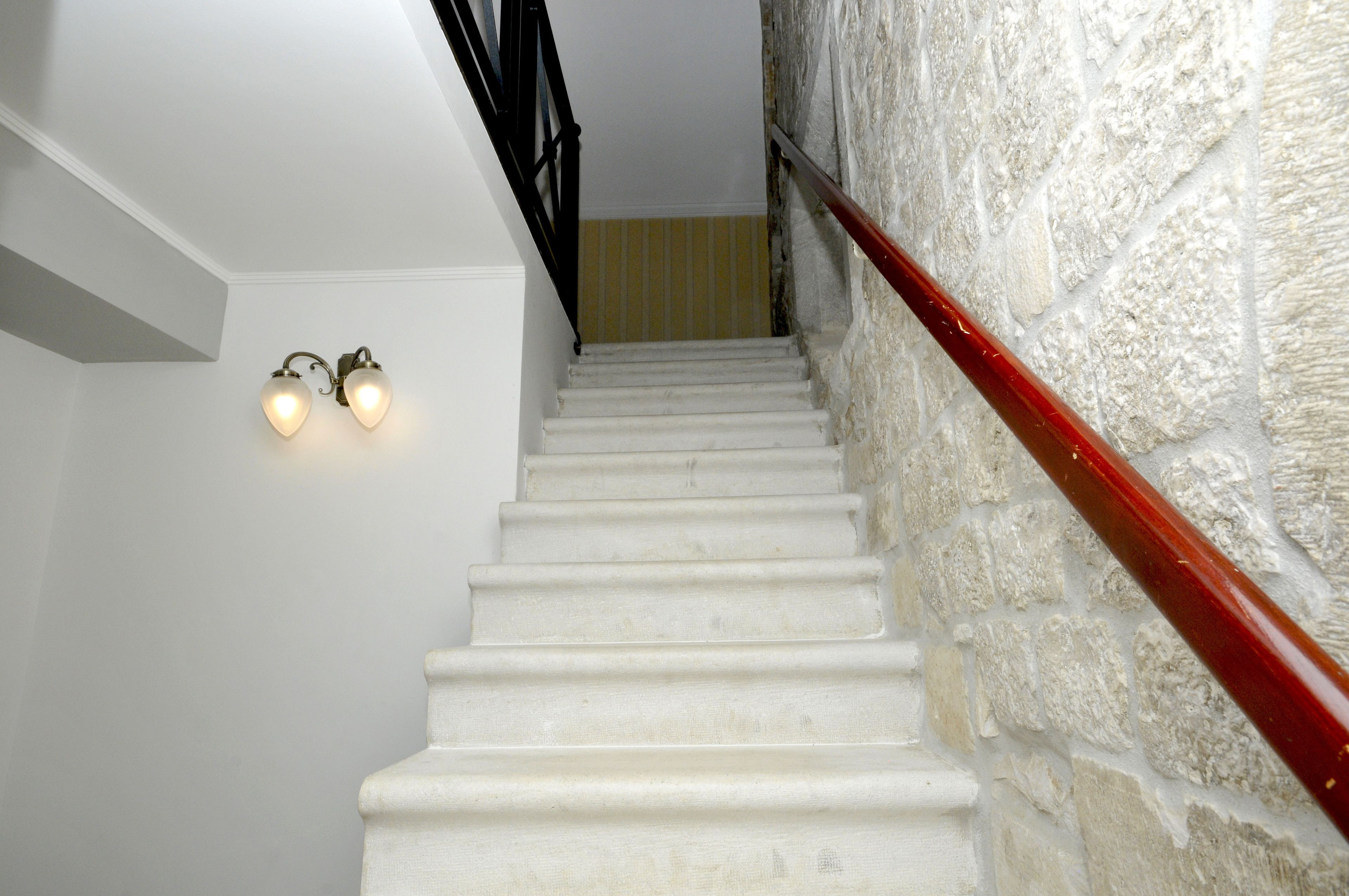 A staircase with white steps, a red handrail, and wall-mounted light fixtures.