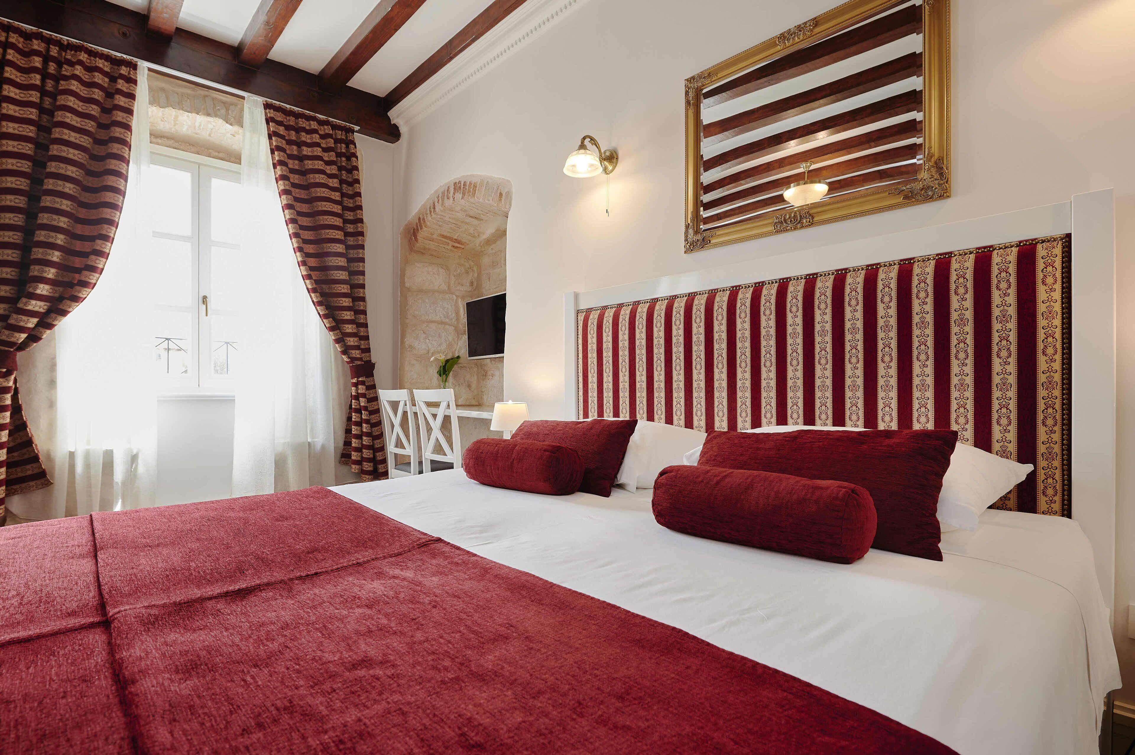 Habitación de hotel con una cama grande, ropa de cama roja, pared de piedra y un televisor.