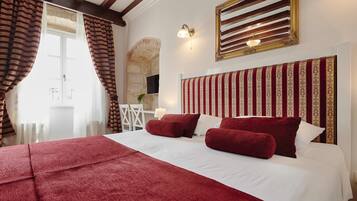Habitación de hotel con una cama grande, ropa de cama roja, pared de piedra y un televisor.