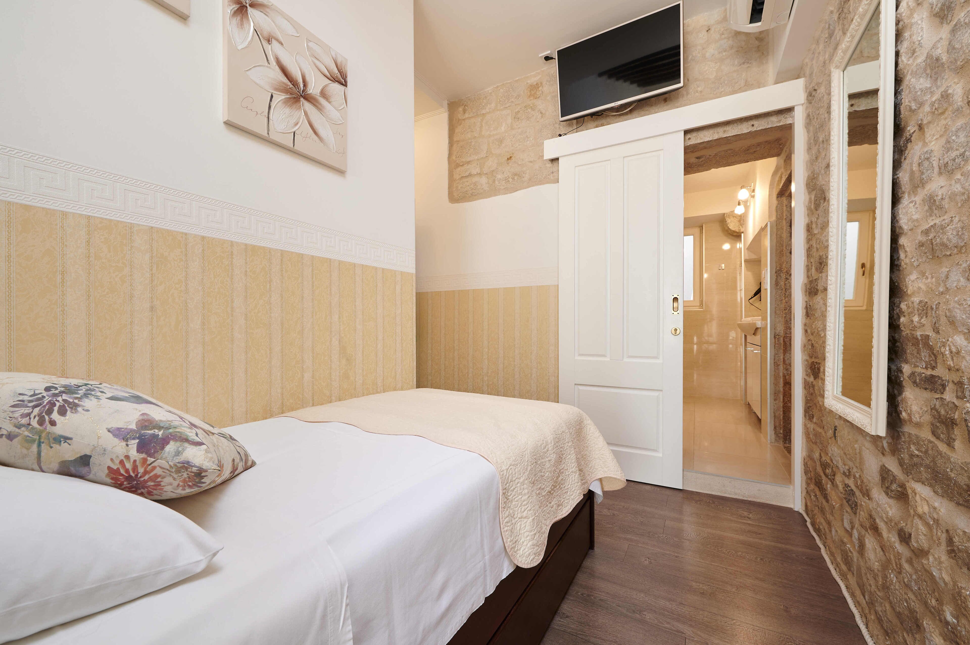 Un dormitorio con una cama, un televisor montado en la pared y una puerta que da a un baño.