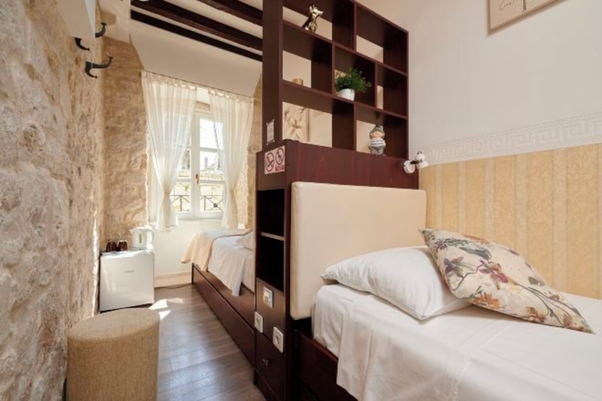 A bedroom with a wooden bunk bed, a bedside table, a small bedside lamp, and a window with curtains.