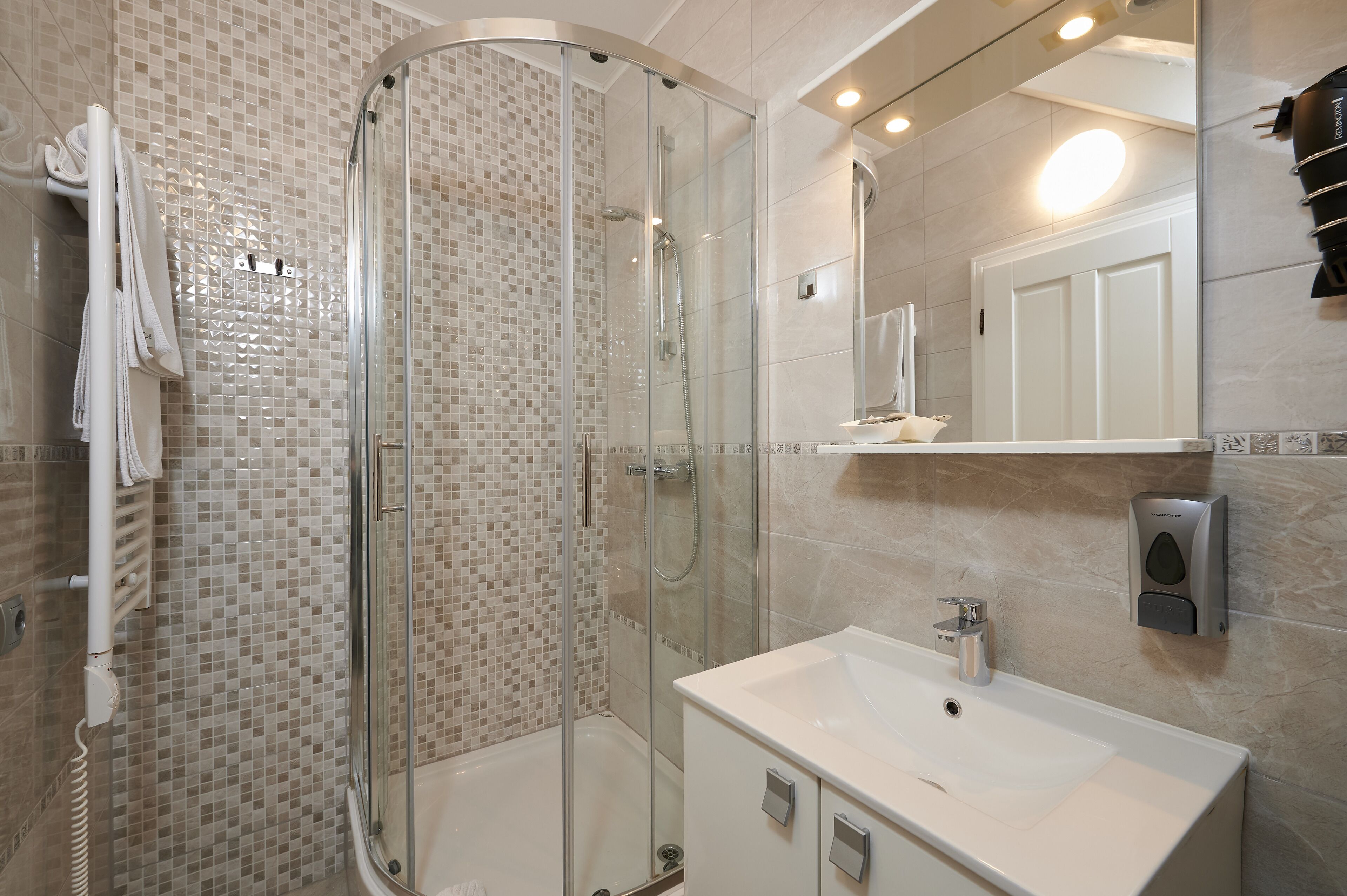 Une salle de bain moderne avec une douche à parois de verre, un lavabo blanc et un miroir au-dessus du lavabo.