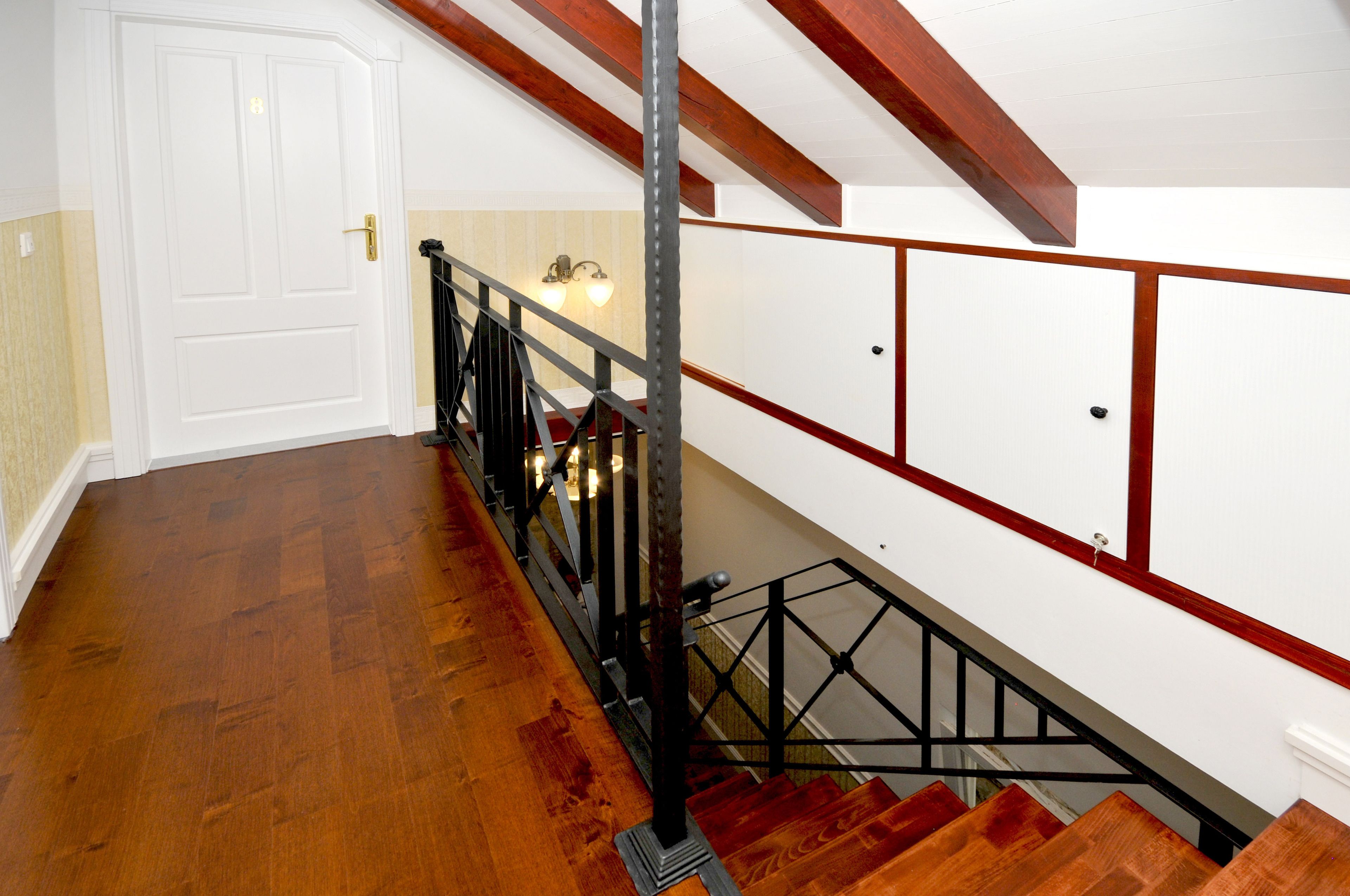 A wooden staircase with a metal railing, white walls, and a door at the top.