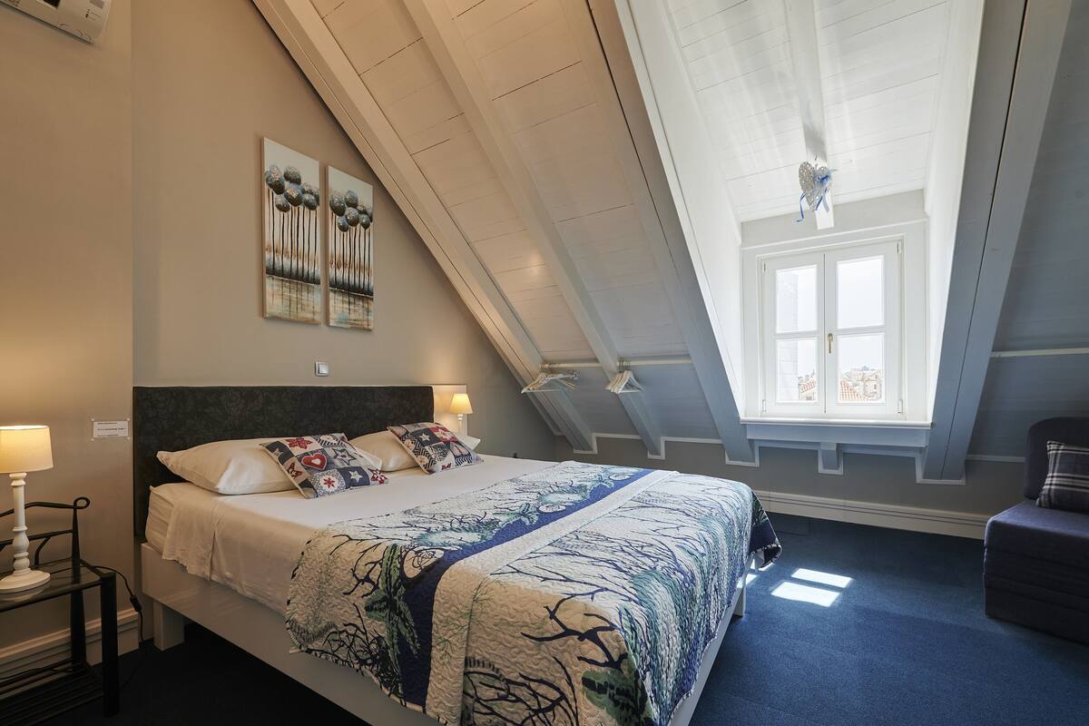 A bedroom with a bed, a nightstand, a window, and a view of the city.