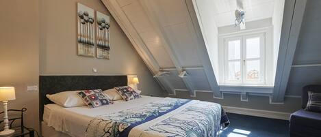 A bedroom with a bed, a nightstand, a window, and a view of the city.