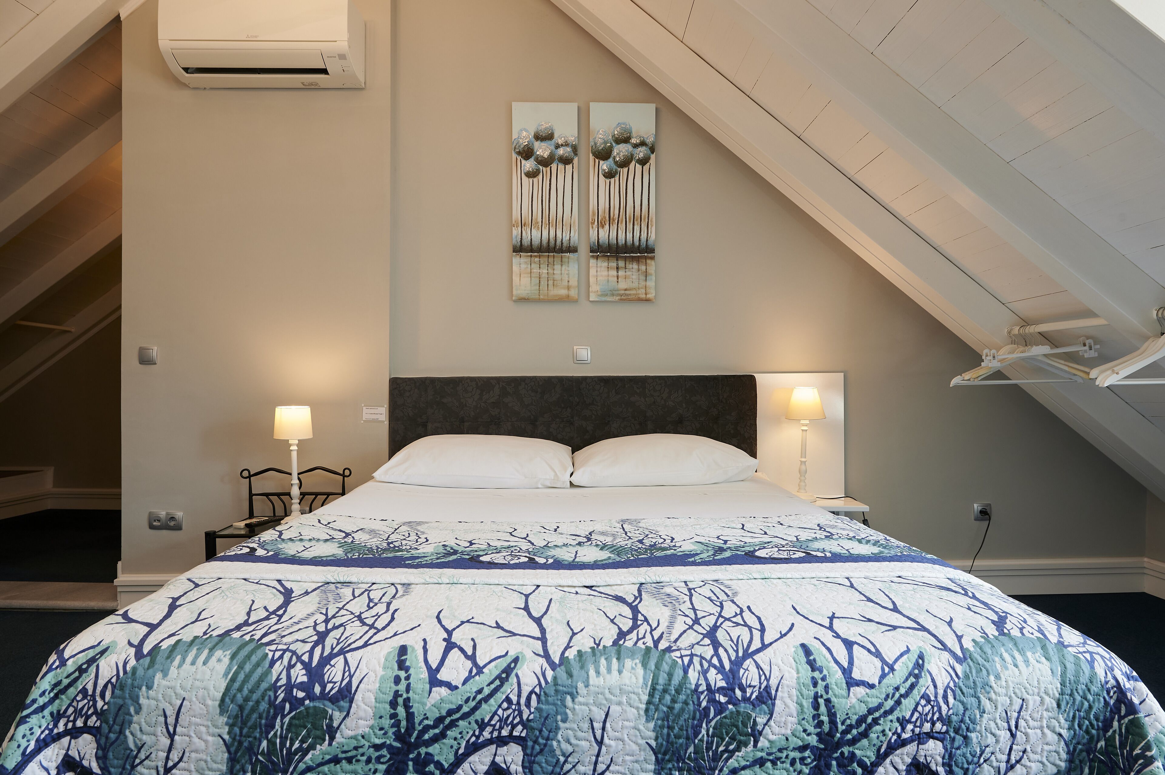 A bedroom with a bed, two bedside lamps, a ceiling fan, and a painting on the wall.