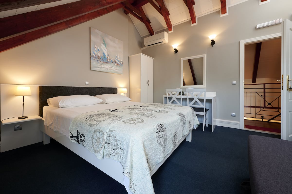 A bedroom with a bed, bedside lamps, a desk, a wardrobe, and a painting on the wall.