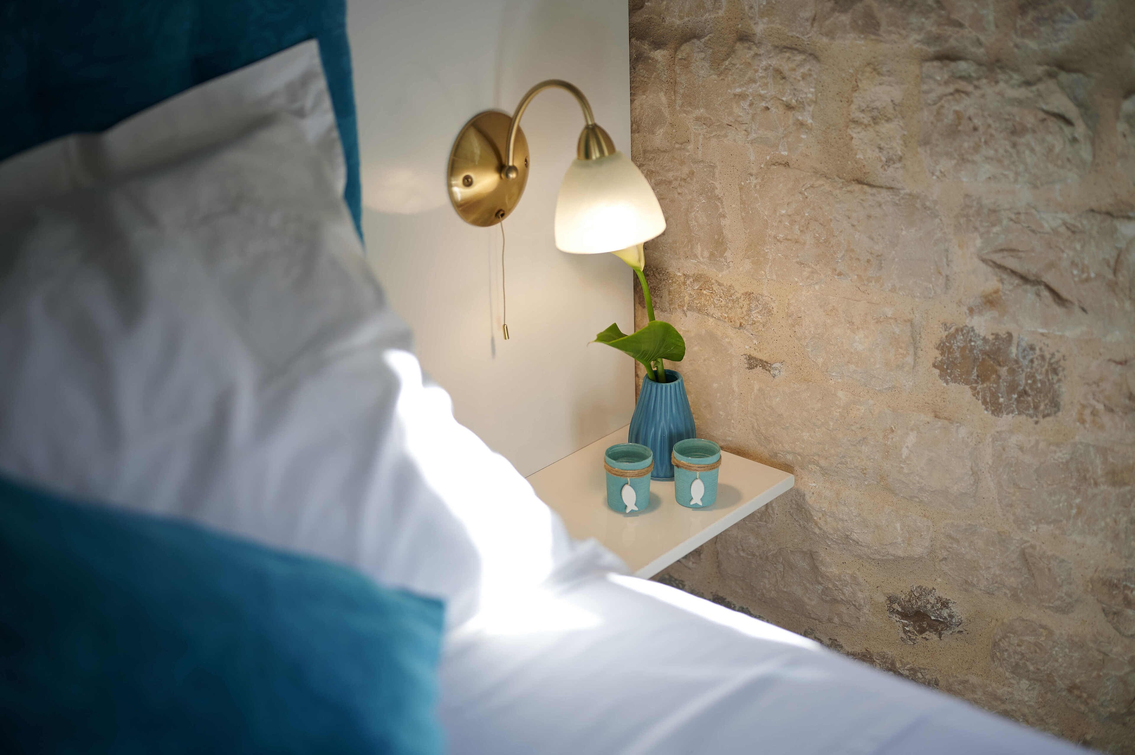 Ein Bett mit weißen Leinen, eine Wandlampe und ein kleiner Tisch mit einer Vase und zwei Kerzenständern.