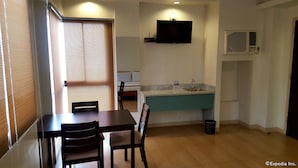 A compact kitchen with a sink, a flat-screen TV mounted above it, and a window with blinds. - M Suites Hotel (Makati)