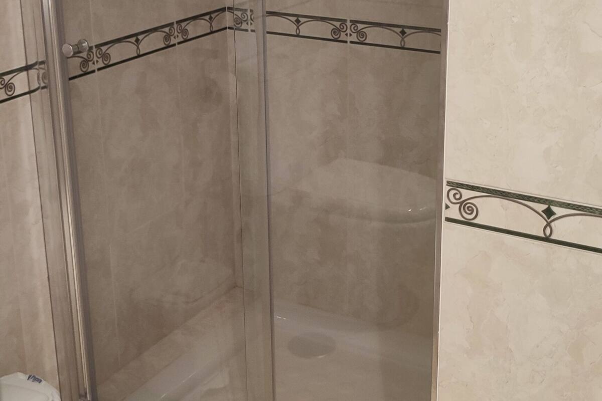 A shower area with a glass door, a hand soap dispenser, and a pink towel hanging on a rack.