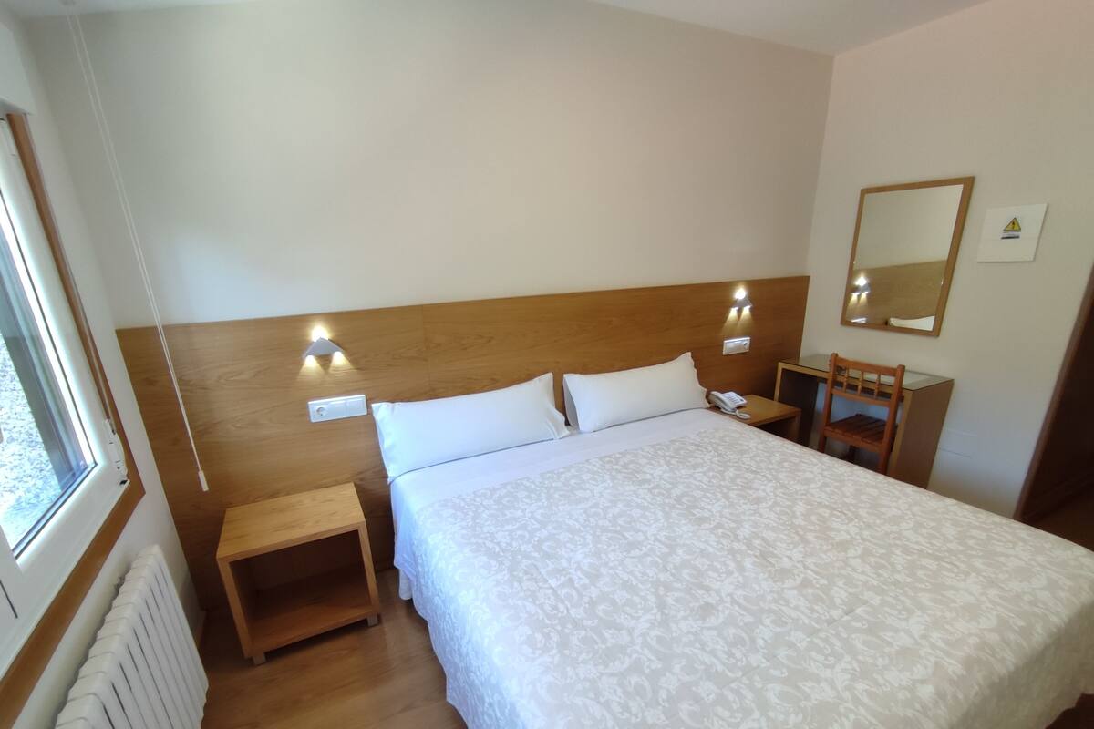 A hotel room with a large bed, bedside tables, a wooden headboard, a mirror, and a radiator.
