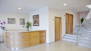 A reception area with a wooden reception desk, a staircase, and a wall with framed artwork. - Hotel Brisa del Mar (O Grove)