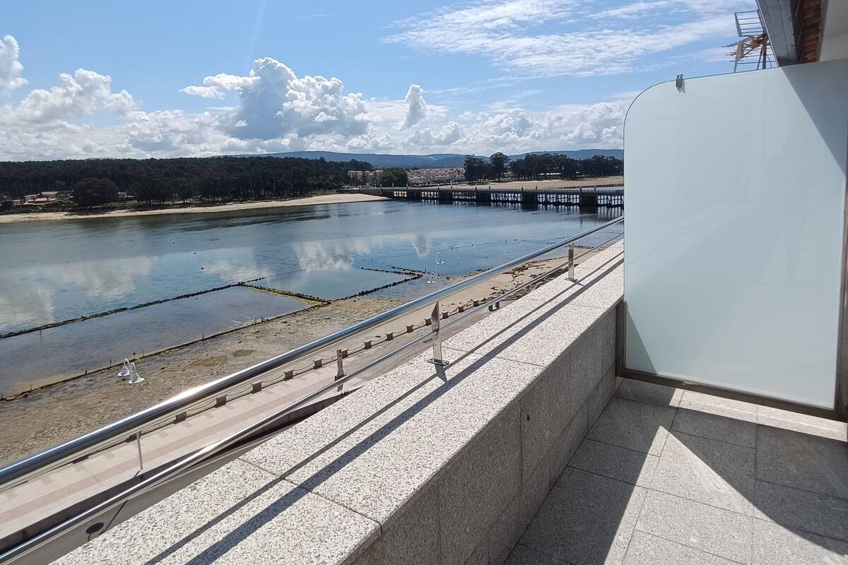 A view from a balcony overlooking a river with a bridge, a sandy beach, and distant hills.