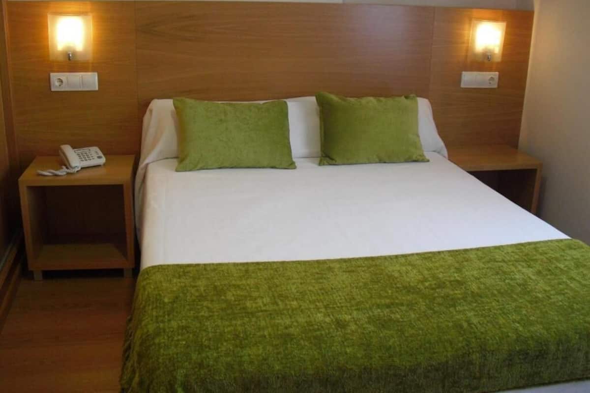 A hotel room with a bed, two nightstands, a telephone, and wall-mounted lights.
