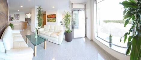 A modern hotel lobby with a glass coffee table, a sofa, and several potted plants.