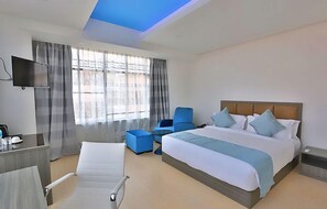 A hotel room with a large bed, a desk, a chair, a TV, and a window with curtains. - City Hotel & Suites (Kathmandu)