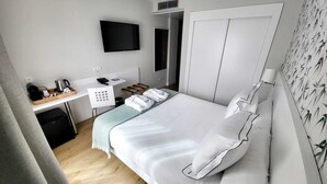 A hotel room with a bed, a desk with a telephone and a coffee maker, a TV mounted on the wall, and a wardrobe.