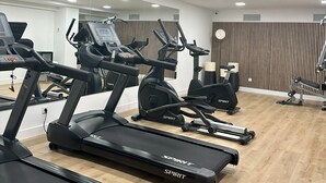 Un gimnasio con cintas de correr, bicicletas estáticas y un espejo grande.