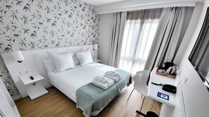 Una habitación de hotel moderna con una cama, mesitas de noche, un escritorio con teléfono y un televisor.