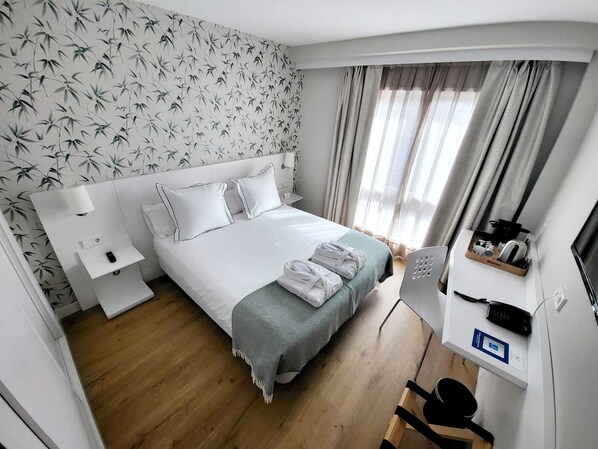 Habitación de hotel con cama, mesita de noche, lámpara y escritorio con teléfono y hervidor.