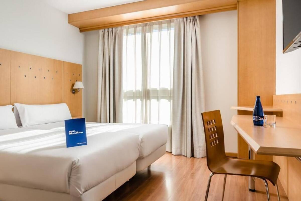 A hotel room with a bed, a desk, a chair, and a window with curtains.