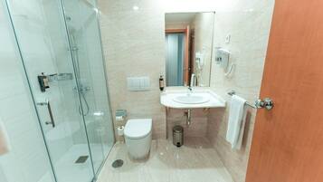 Un baño moderno con ducha de vidrio, un lavamanos blanco y un inodoro.