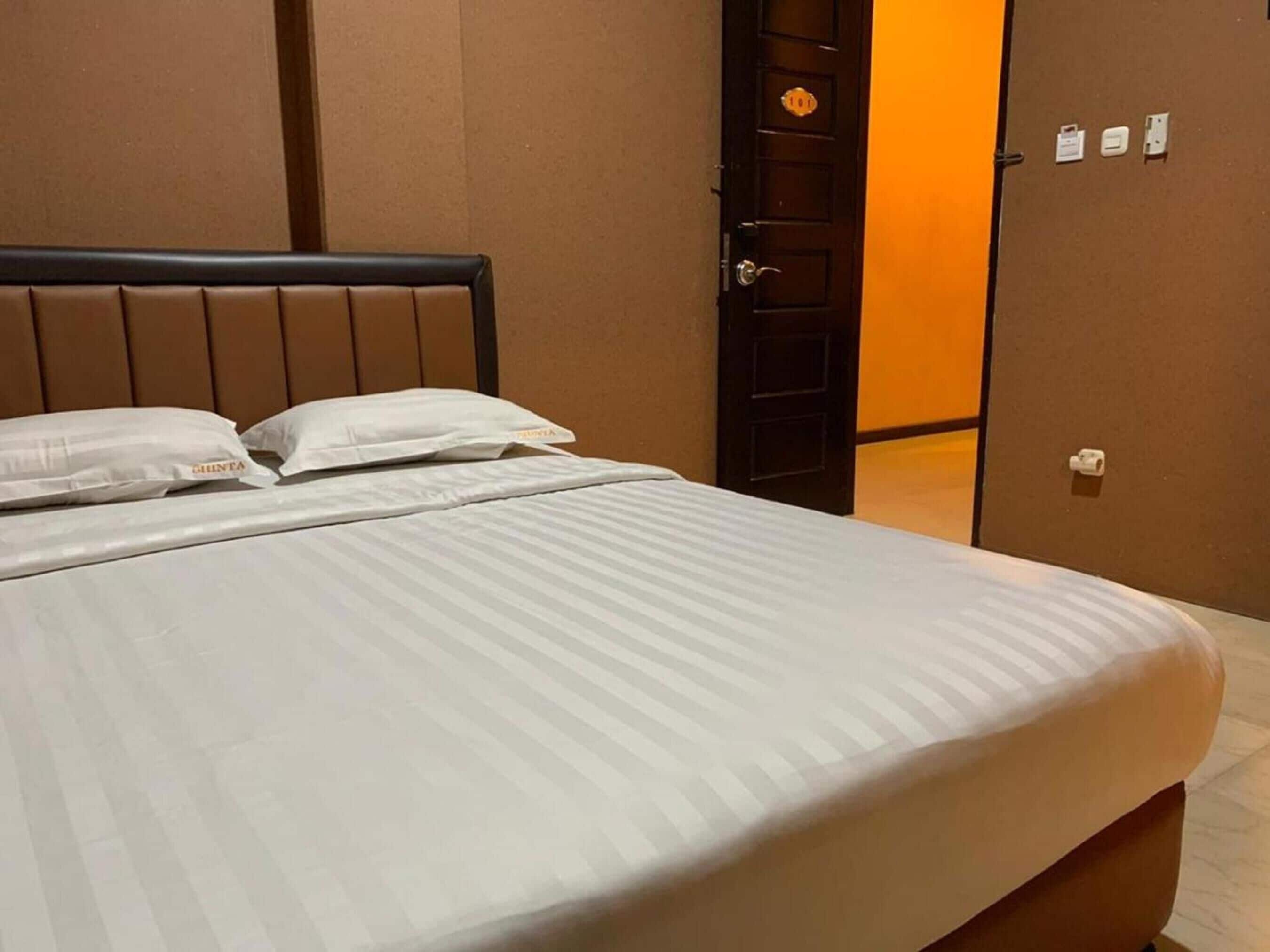 A hotel room with a bed, pillows, and a door.