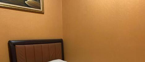 A single bed with a headboard, a white pillow, and a white bedspread in a room with orange walls.