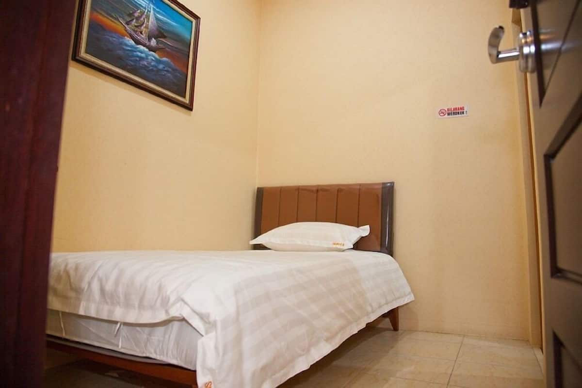 A small, single-bed room with a wooden headboard, a white bedspread, and a framed picture on the wall.