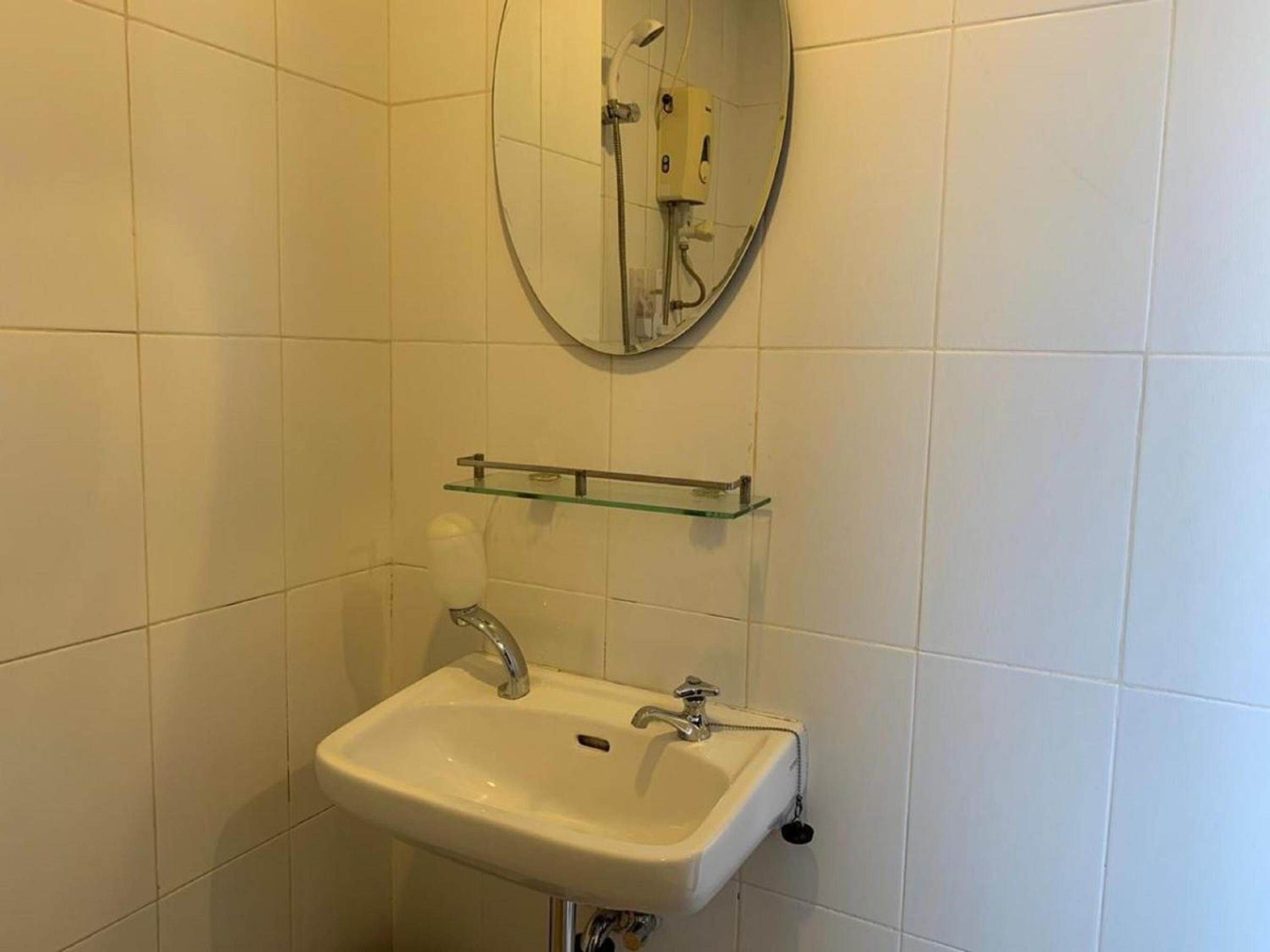 Een badkamer met een witte wastafel, een glazen plank erboven en een spiegel boven de plank.