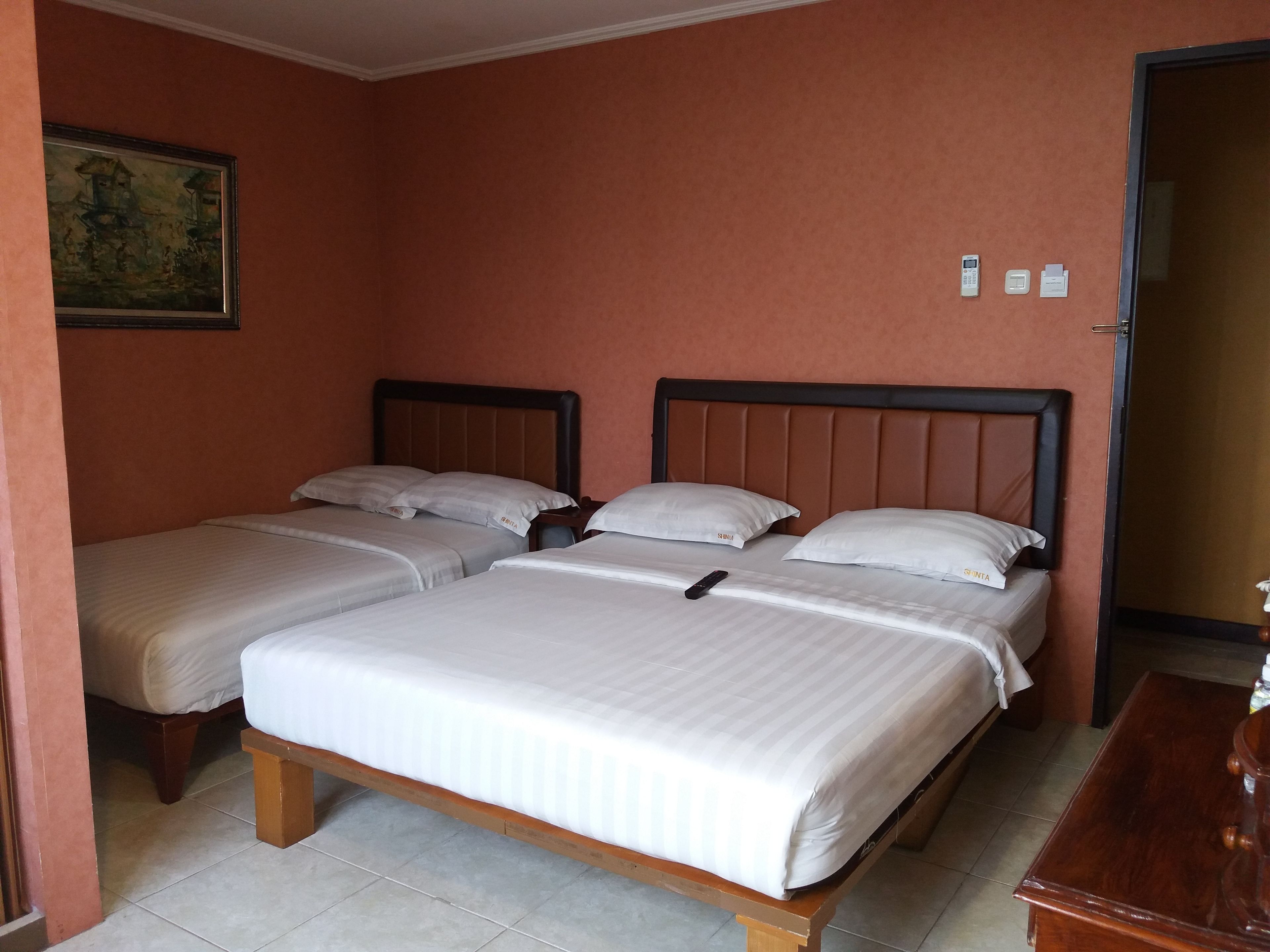 Une chambre d’hôtel avec deux lits simples, une tête de lit en bois, un petit bureau et un tableau au mur.