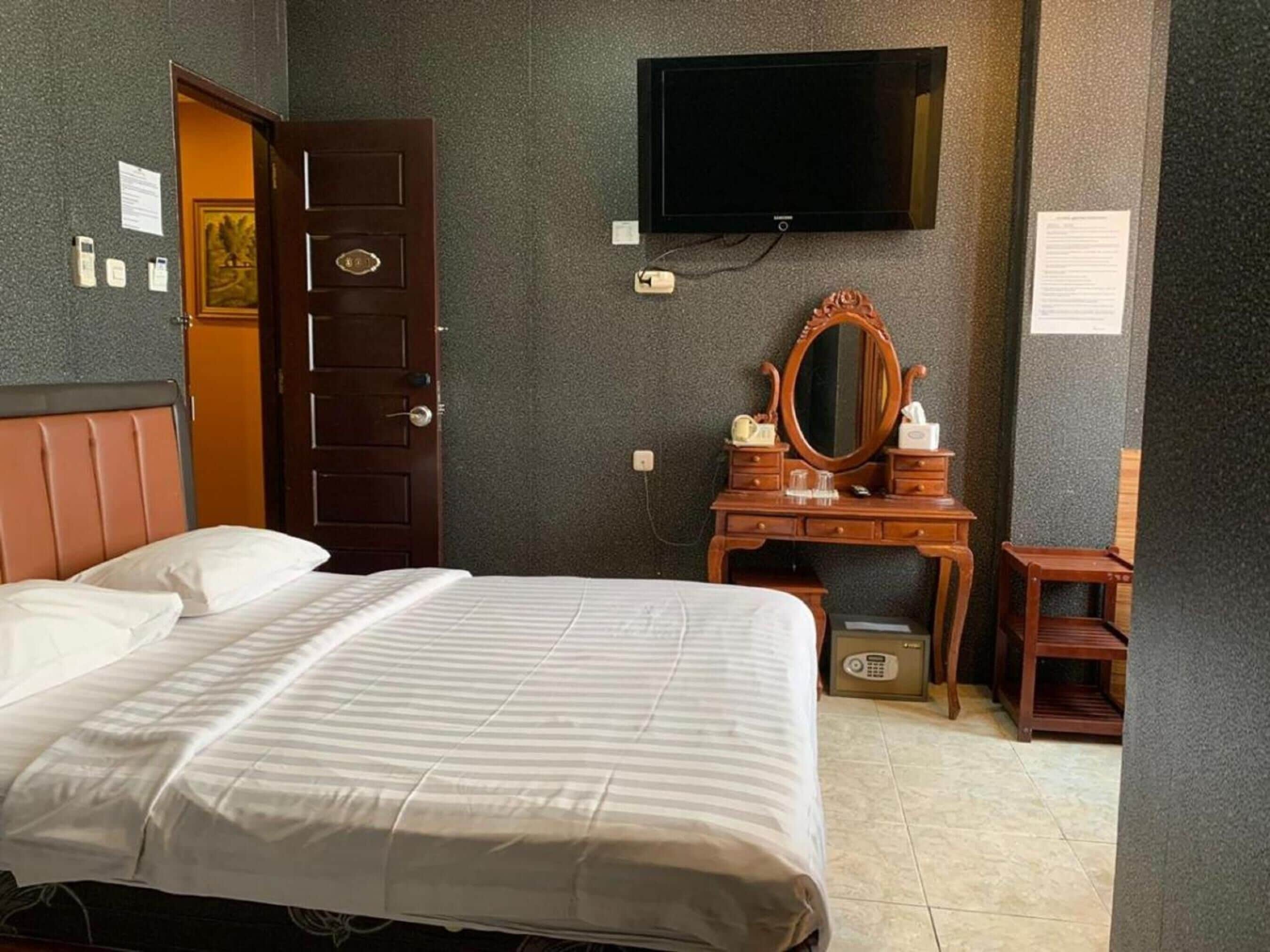 A hotel room with a bed, a wooden dresser, a television mounted on the wall, and a door.