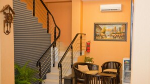 A staircase with a black railing, a clock on the wall, a framed painting, and a seating area with chairs and a small table. - Rumah Shinta (Jakarta)