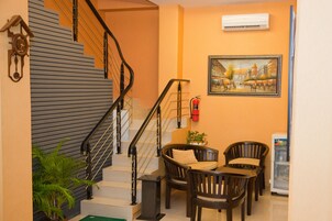 Uma escadaria com guarda-corrimão preto, um relógio na parede, um quadro emoldurado e um espaço de estar com cadeiras e uma mesa pequena.