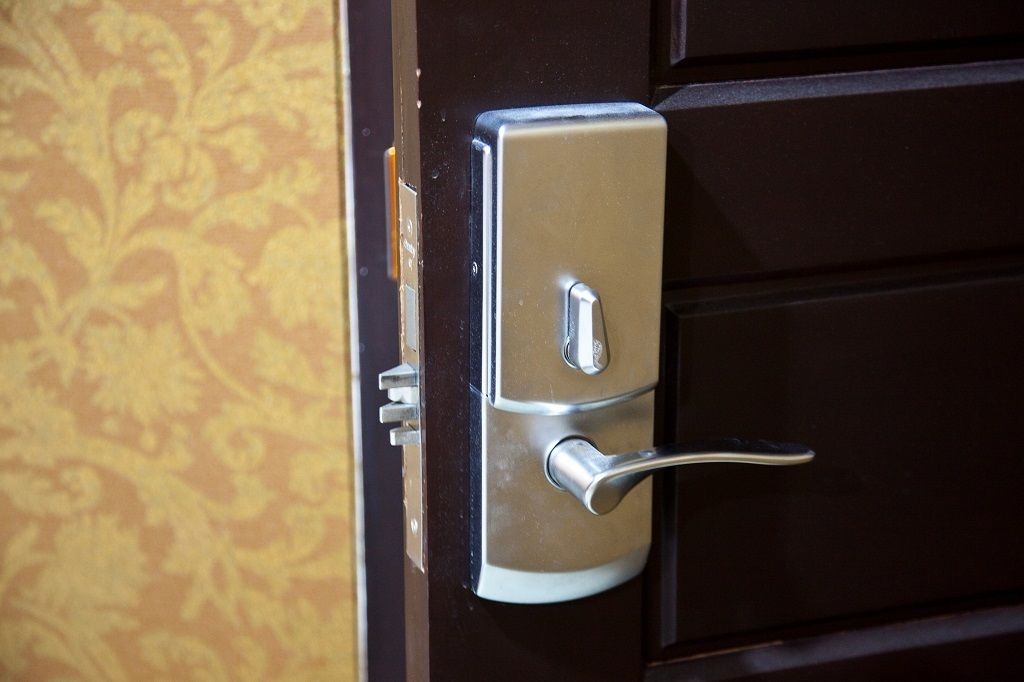 Une porte dotée d’une poignée métallique et d’un trou de serrure, située dans une pièce dont les murs sont recouverts d’un papier peint à motifs.