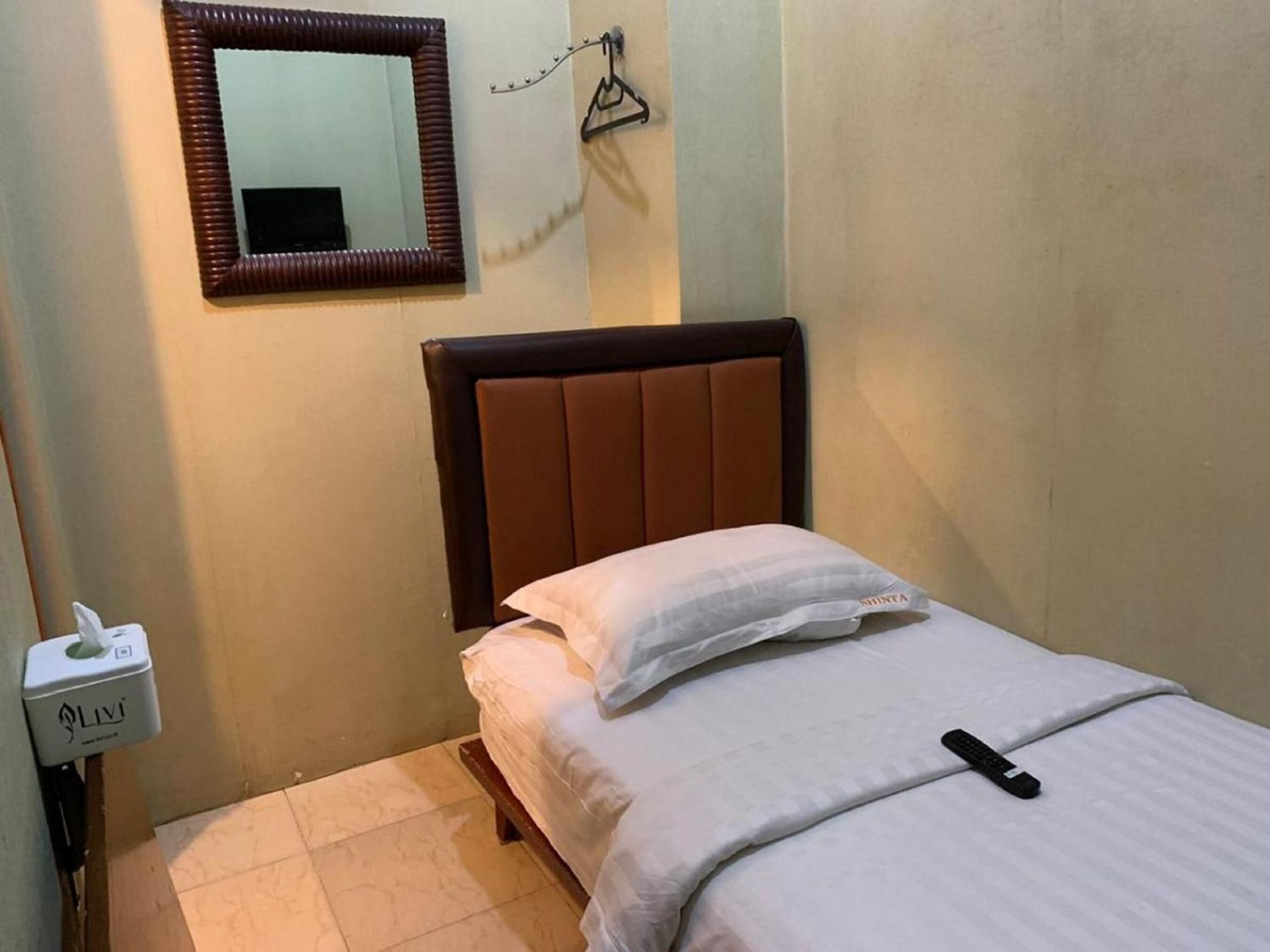 Een klein, netjes opgemaakt bed met een bruin hoofdbord, een wit kussen en een afstandsbediening op het bed.