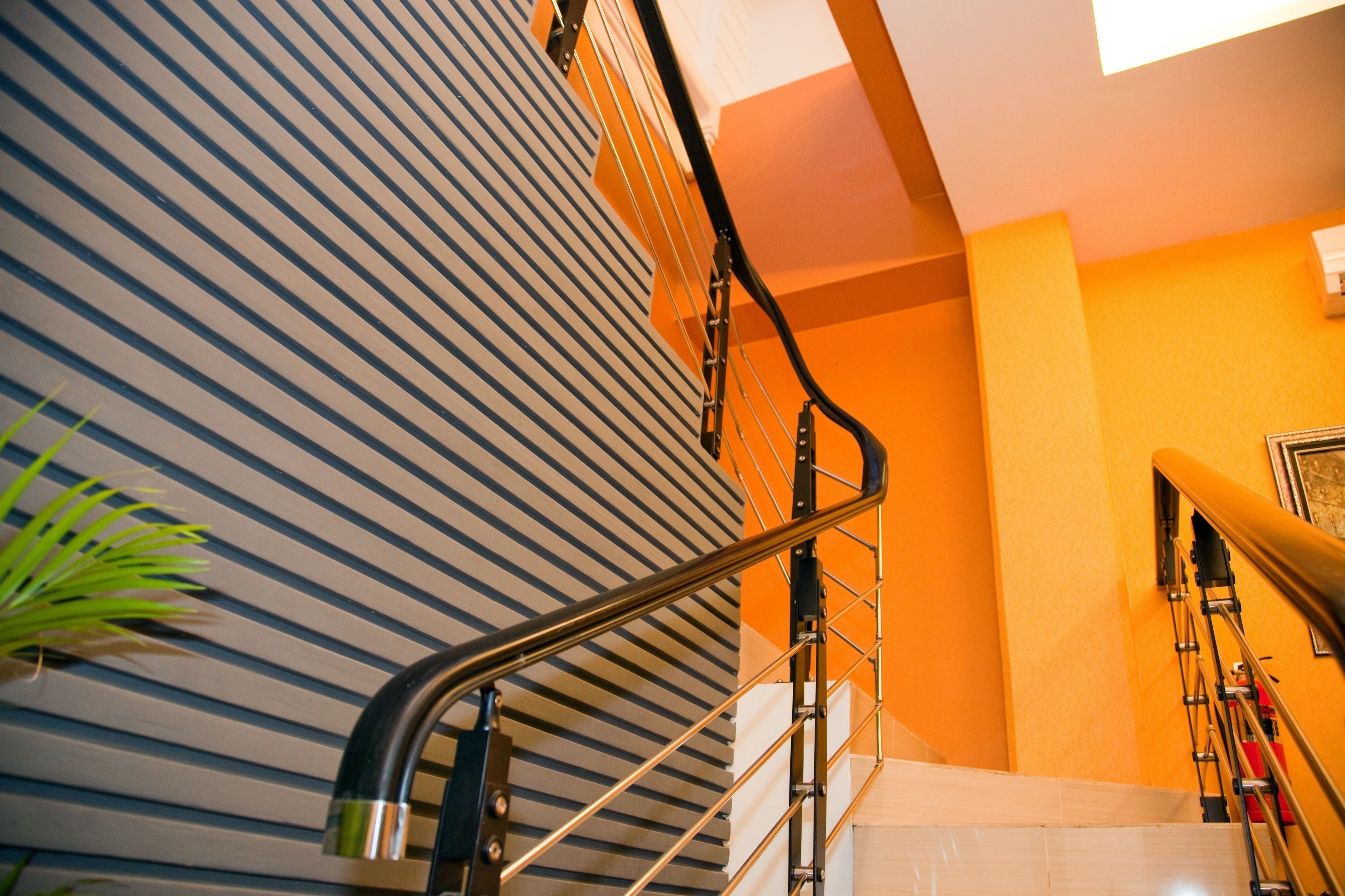 A staircase with a metal handrail, striped wall, and a potted plant.