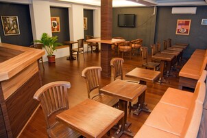 Um restaurante com mesas e cadeiras de madeira, um vaso de planta e obras de arte nas paredes.