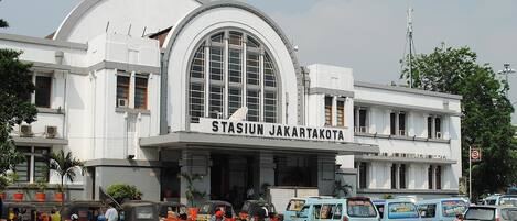 A large building with a sign reading "STASIUN JAKARTA" and multiple tuk-tuks parked in front.