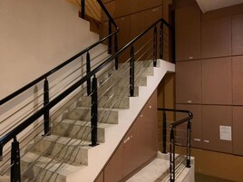 Uma escadaria com guarda-corrimão de vidro, degraus bege e paredes castanhas.