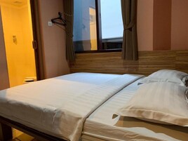 Quarto de hotel com uma cama, janela com cortinas e cabeceira de madeira.