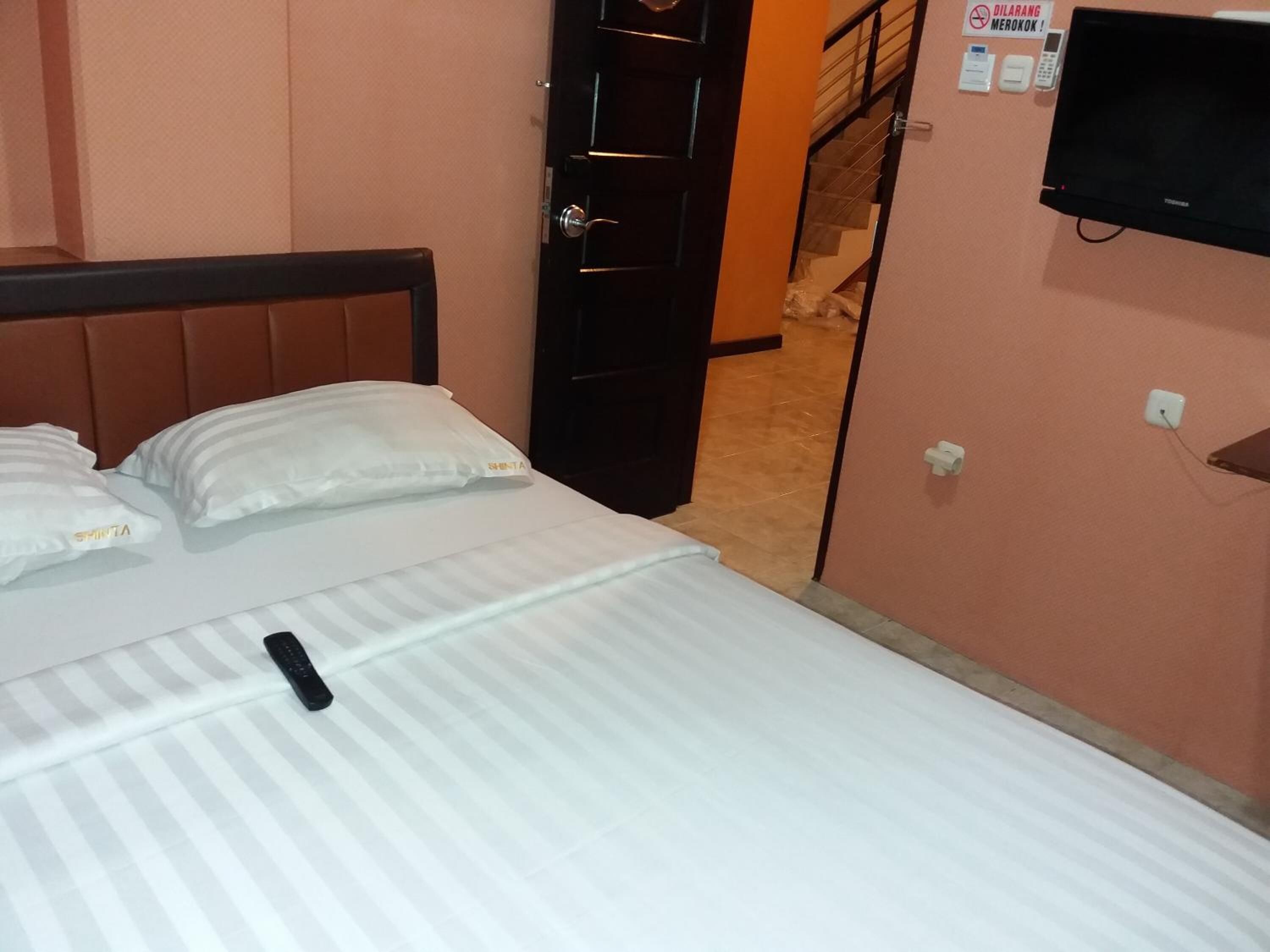A hotel room with a bed, pillows, a TV, and a door leading to a staircase.
