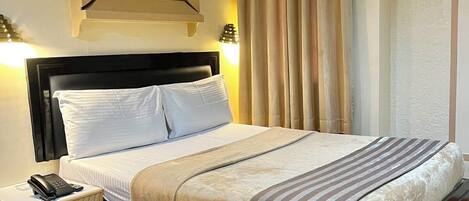 A hotel room with a bed, bedside table, and an air conditioning unit.