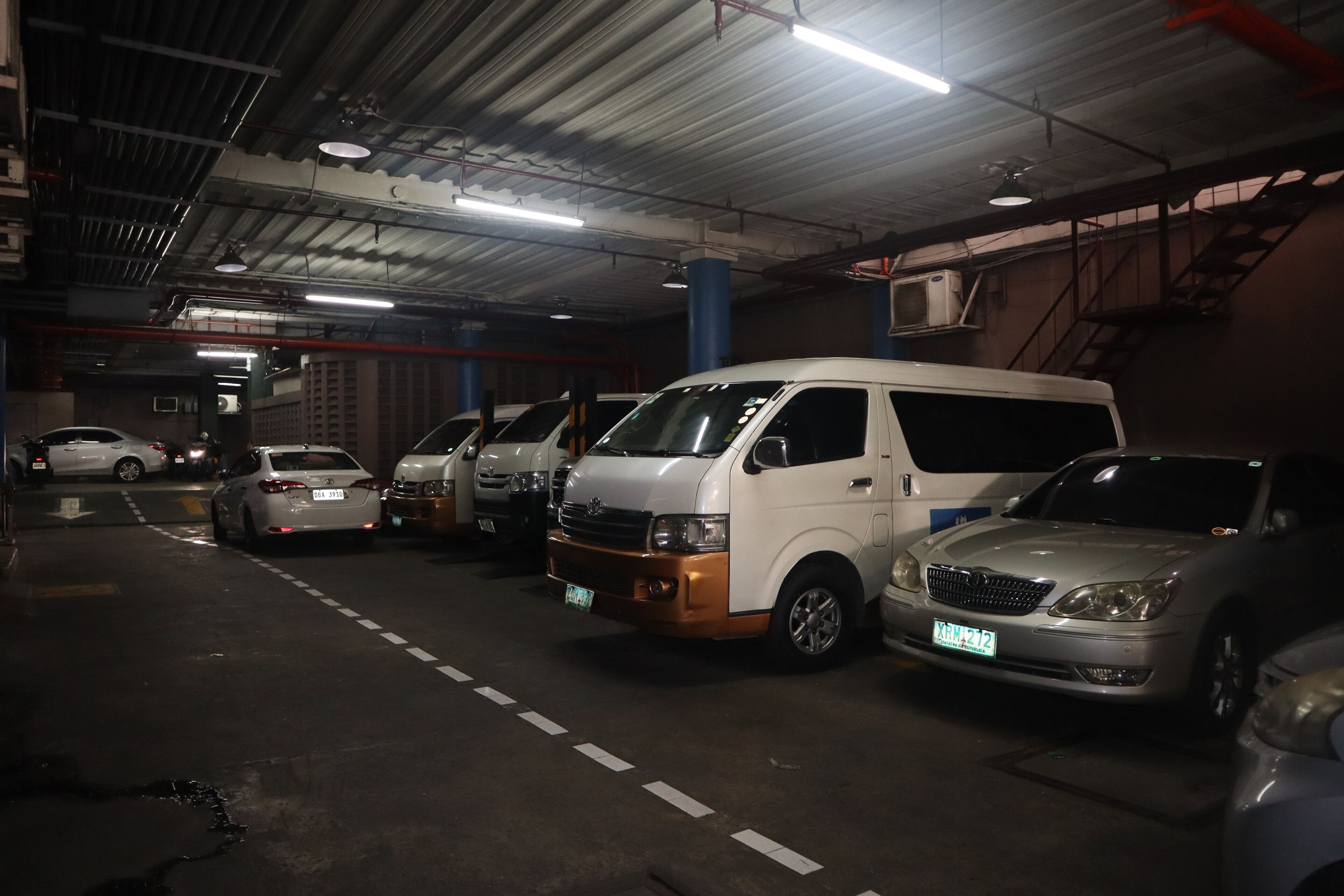 A parking garage with multiple vehicles, including a white van and several cars.