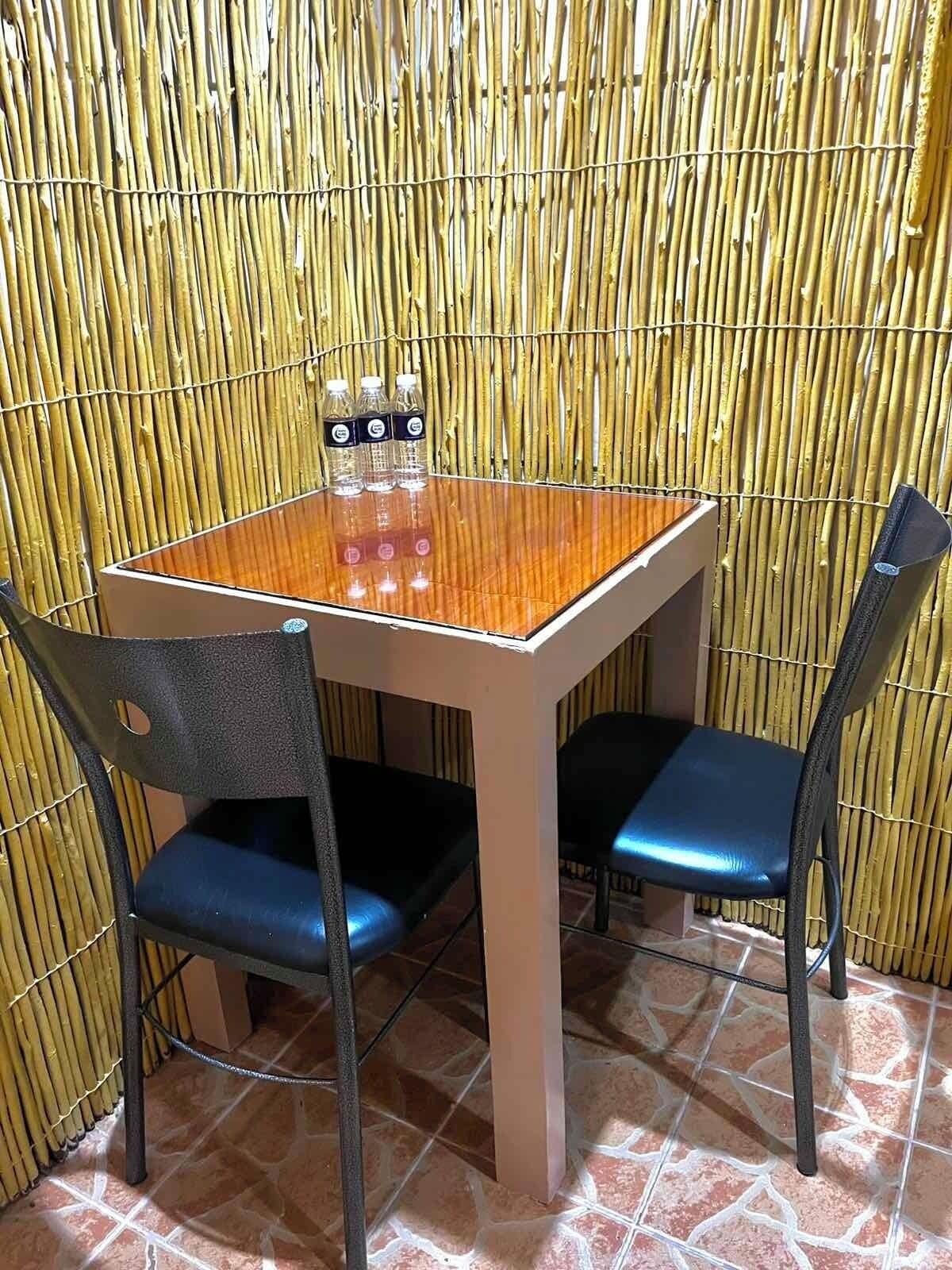 A small dining area with a bamboo wall, a wooden table, and two blue chairs.