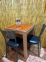 A small dining area with a bamboo wall, a wooden table, and two blue chairs.