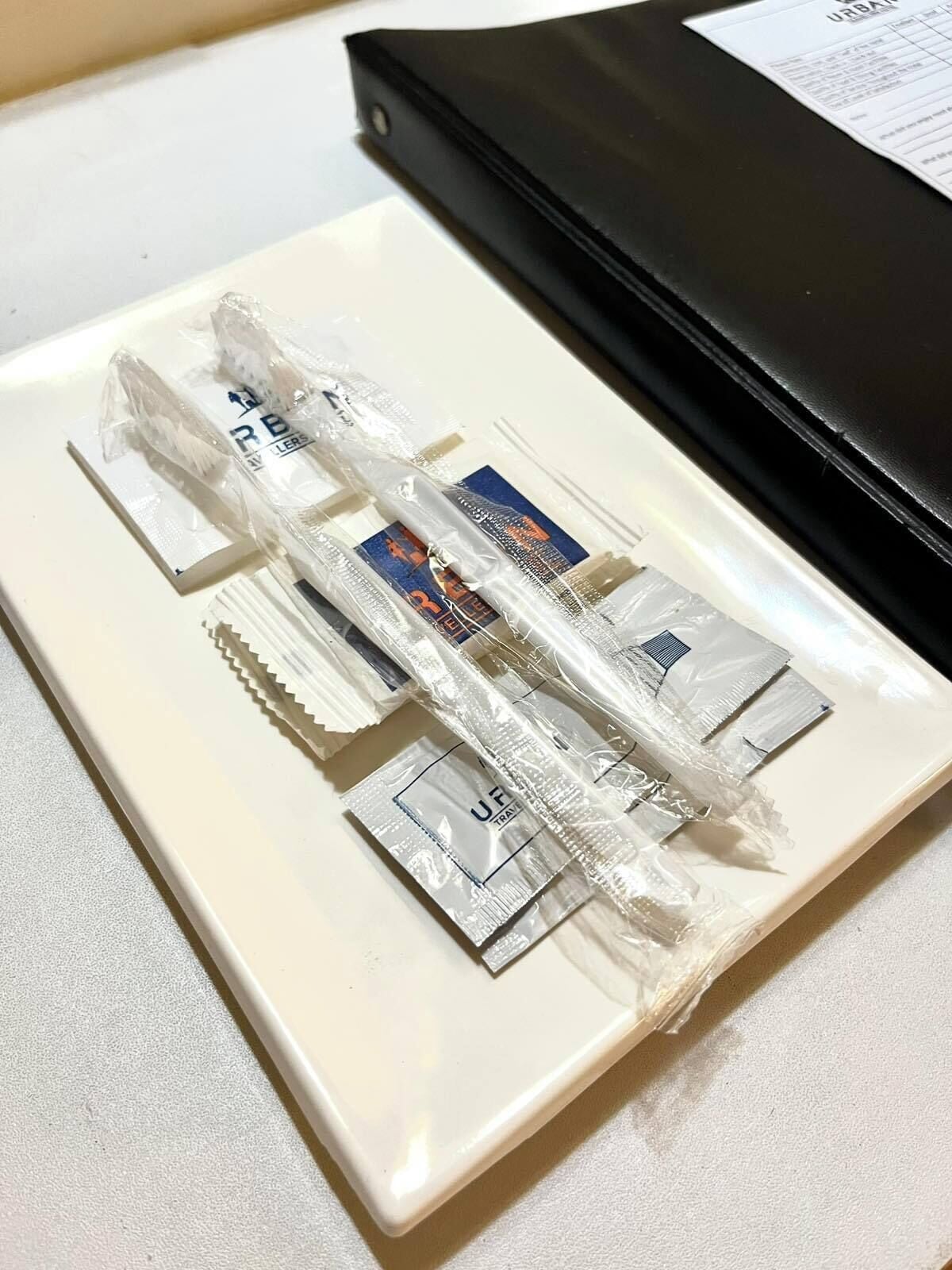 A white plate with several packets of travel-sized toiletries, including a toothbrush and toothpaste, on a white countertop.