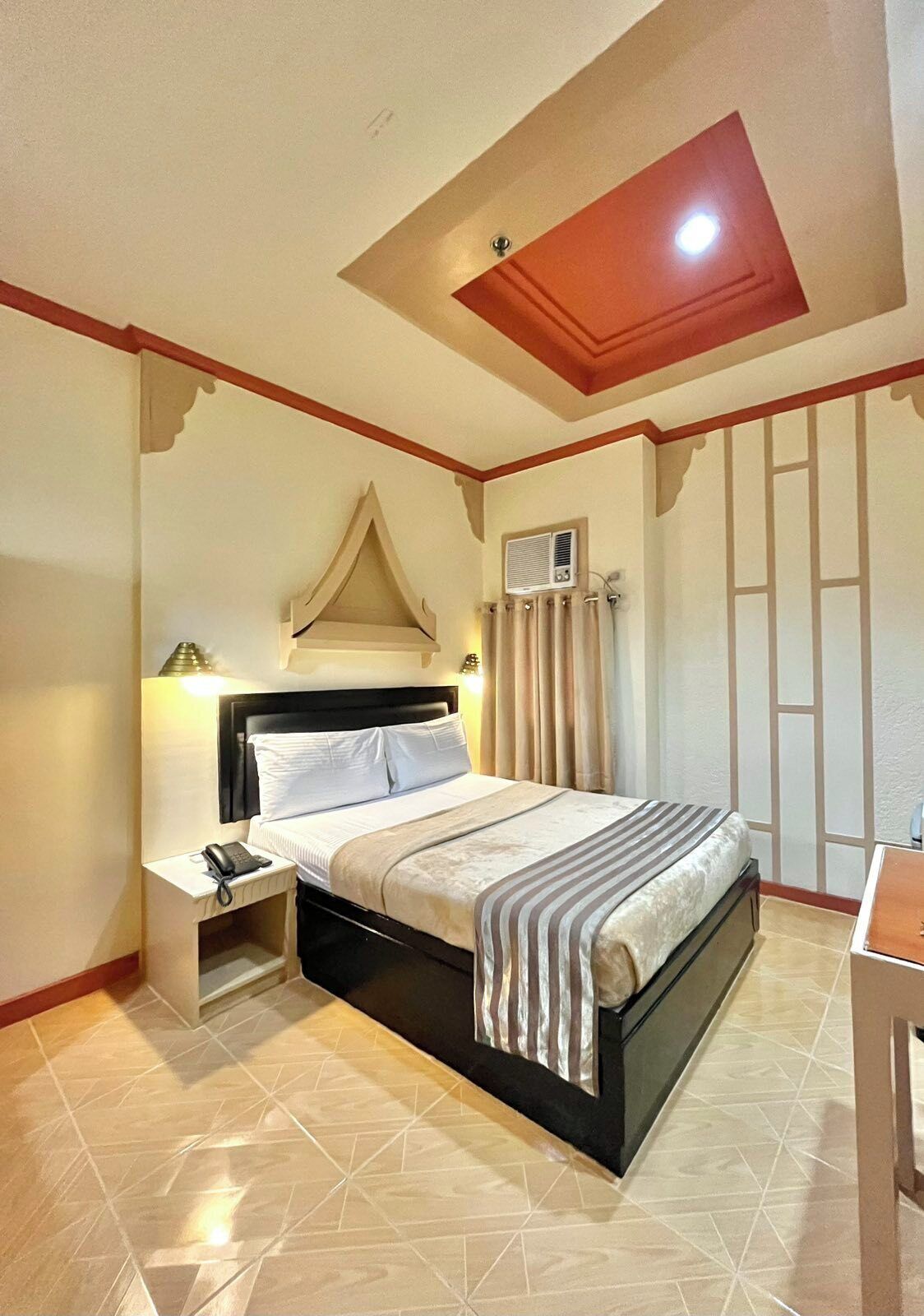 A hotel room with a bed, bedside table, and an air conditioning unit.