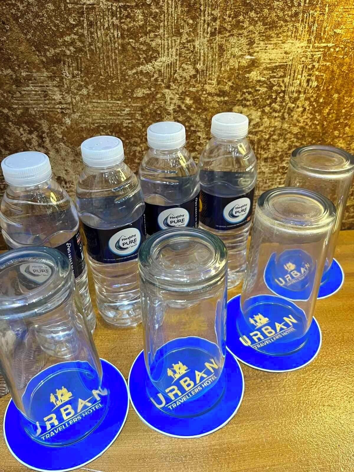 A collection of water bottles and glasses with the "Urban Travellers Hotel" logo on blue coasters.