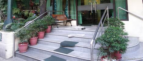 A hotel entrance with a staircase, potted plants, and a bench.